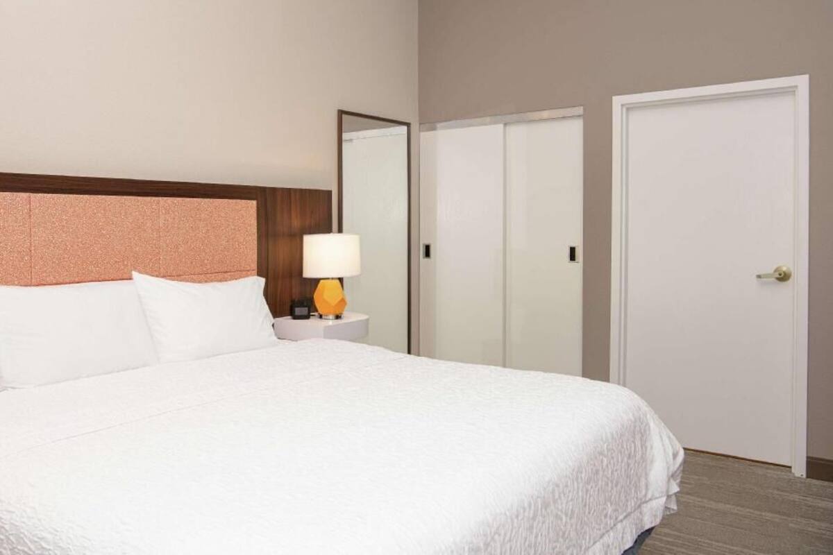 Une chambre d’hôtel avec un grand lit, une table de chevet avec une lampe, une armoire et une porte.