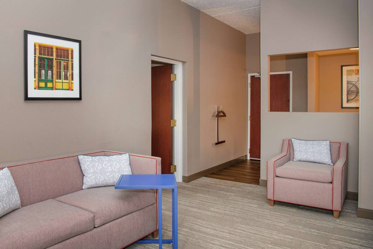 Une chambre d’hôtel avec un canapé rose, une petite table bleue, une chaise et un tableau encadré au mur.