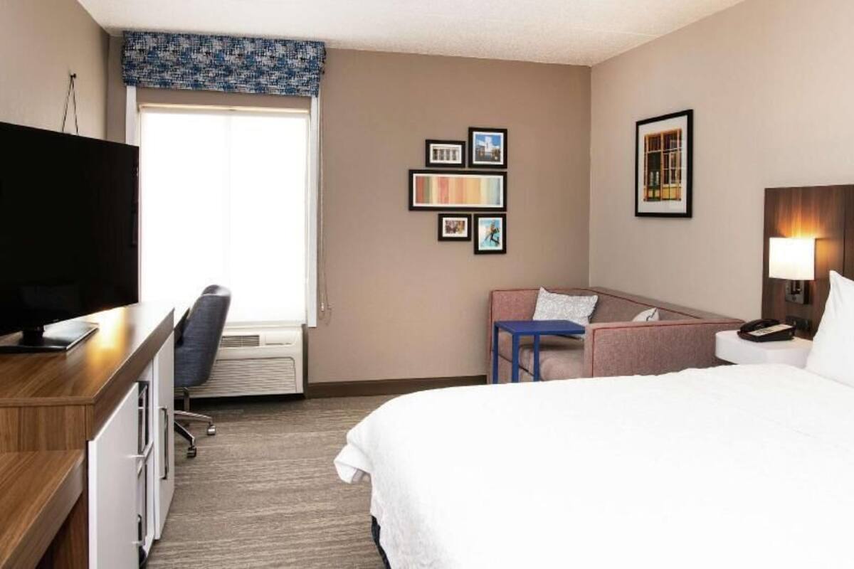 Une chambre d’hôtel avec un lit, un bureau, une chaise, une télévision et des tableaux encadrés au mur.
