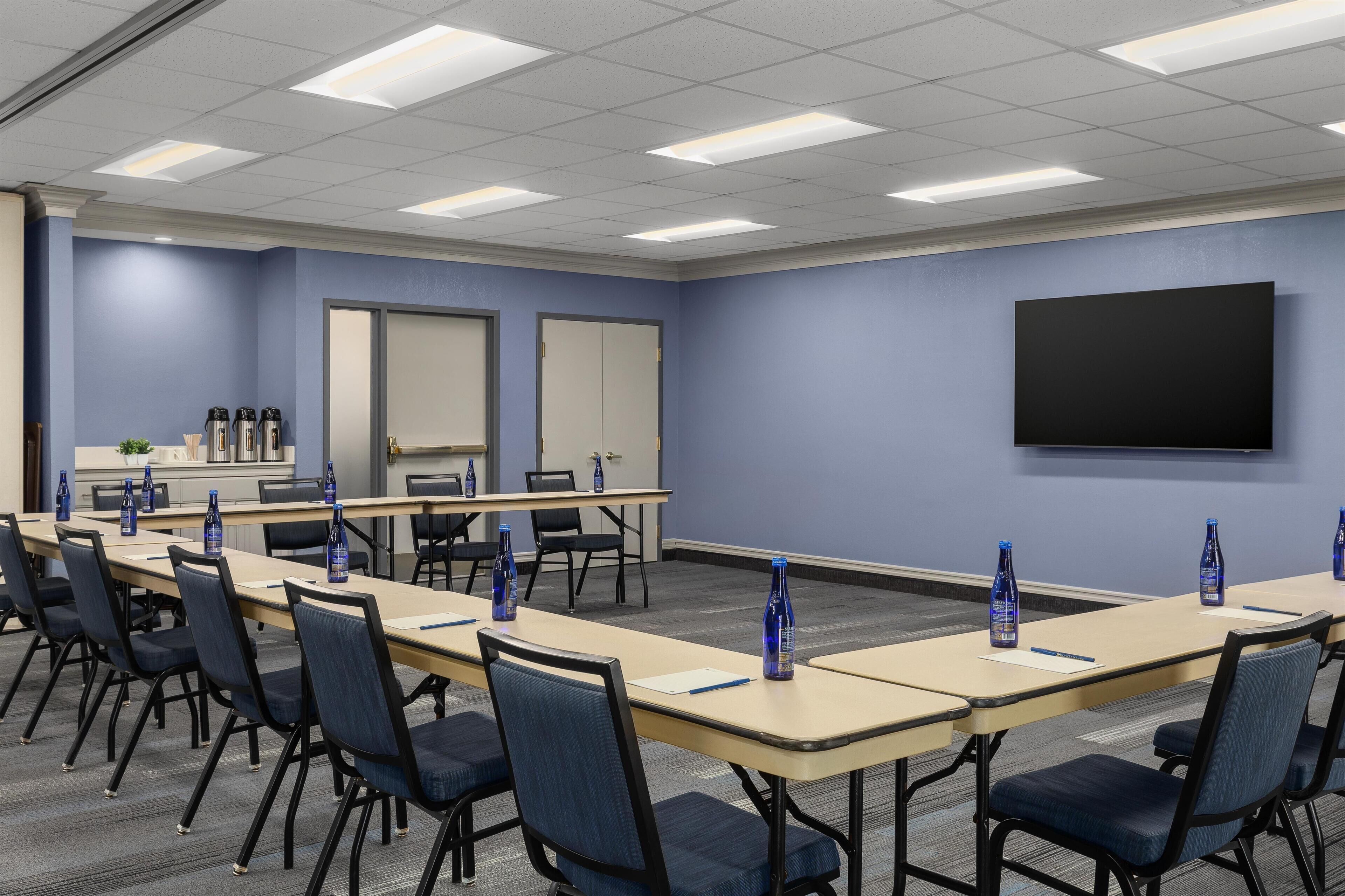A conference room with a long table, chairs, a projector screen, and water bottles.