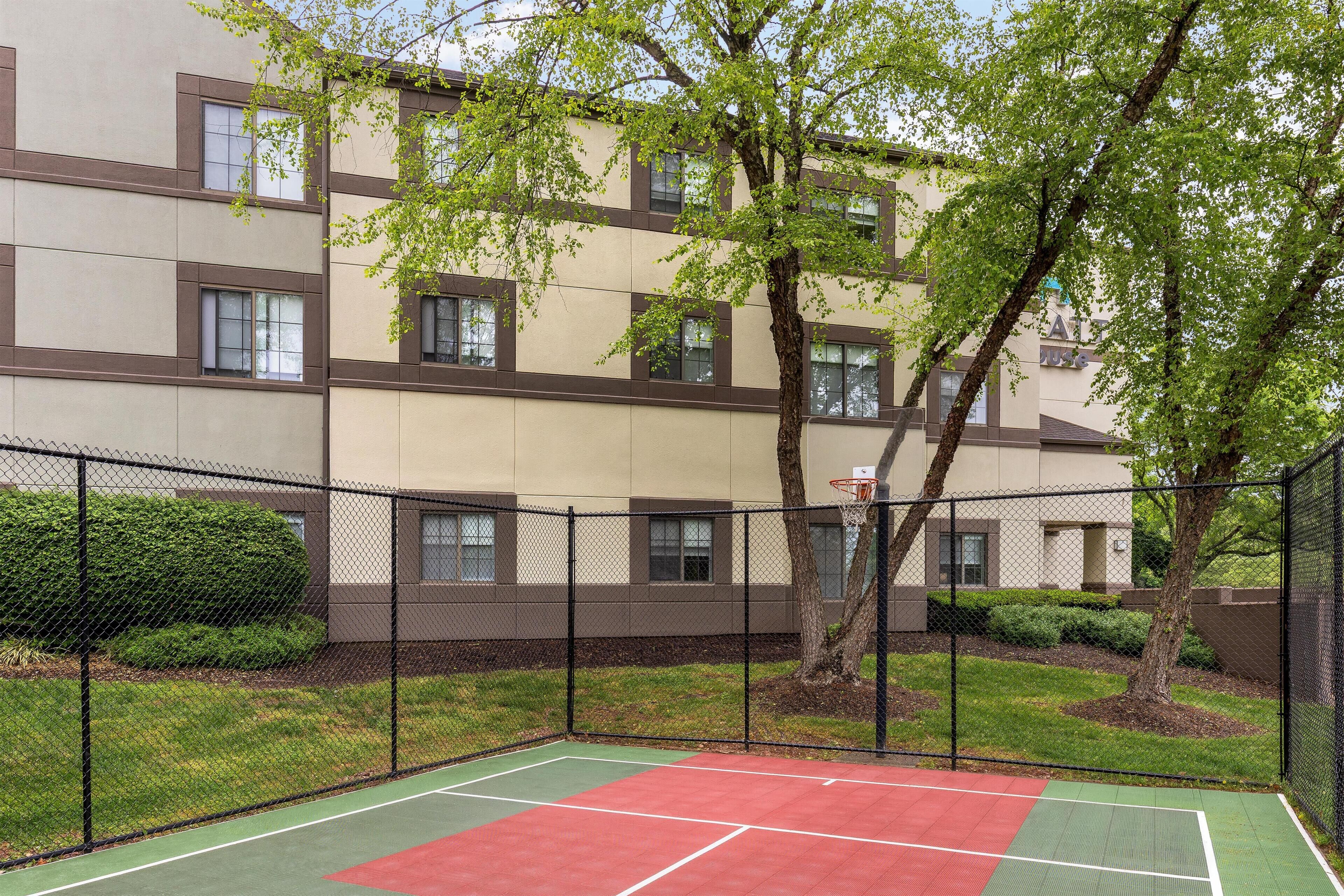 A multi-story building with a basketball court enclosed by a fence.