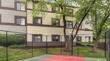 A multi-story building with a basketball court enclosed by a fence.