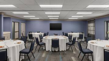 A conference room with round tables, chairs, a flat-screen TV, and a window with curtains.