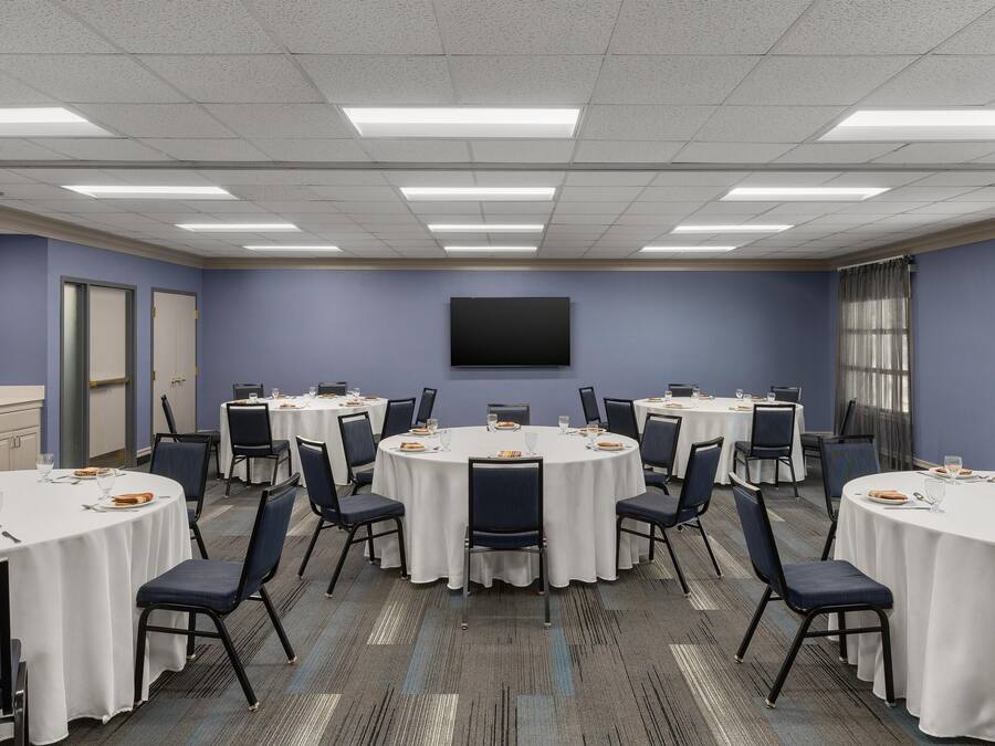 A conference room with round tables, chairs, a flat-screen TV, and a window with curtains.