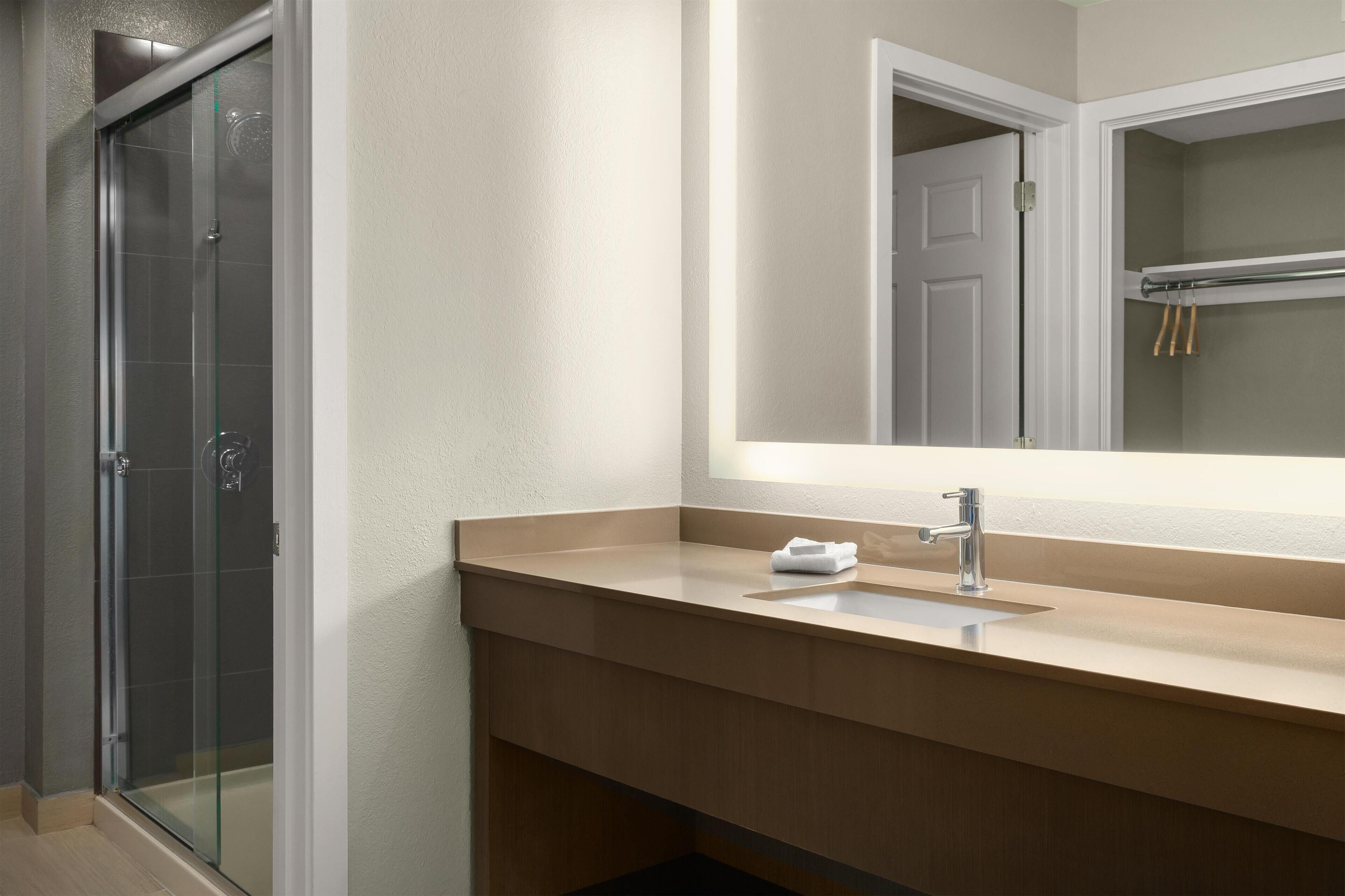 Une salle de bain avec une douche à parois de verre, un lavabo avec un miroir au-dessus et une serviette posée sur le lavabo.