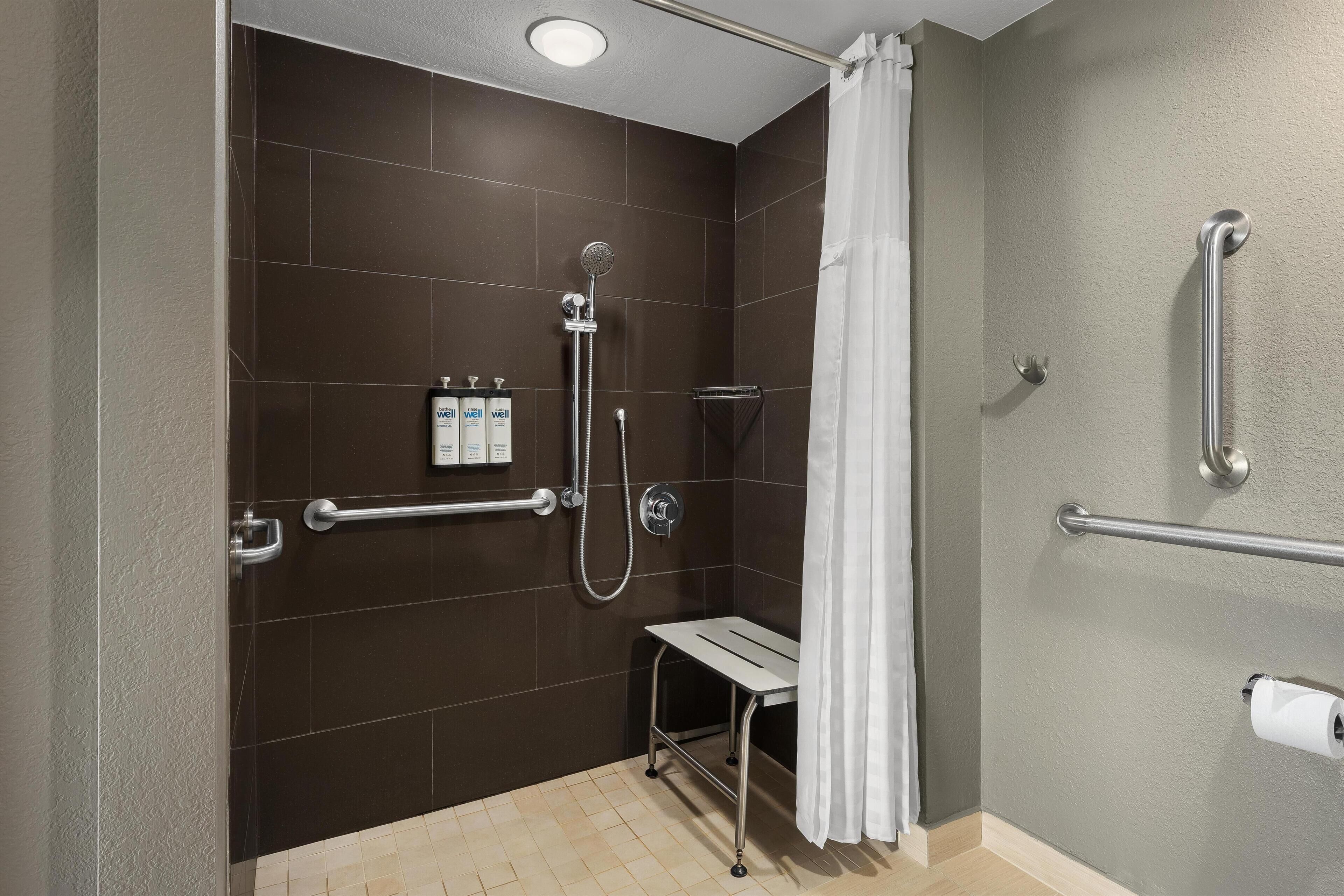 En brusekabine med gelænder, håndbruser og toiletpapirholder.