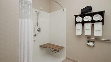 A shower with a glass door, a towel rack with folded towels, and a small wooden shelf.