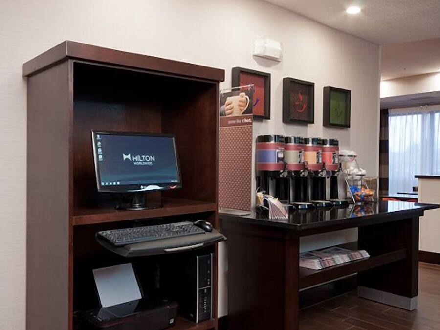 Un mostrador de recepción de hotel con una computadora, una estación de café y obras de arte enmarcadas en la pared.