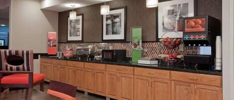 Cocina de hotel moderna con armarios de madera, una cafetera y una exposición de frutas.