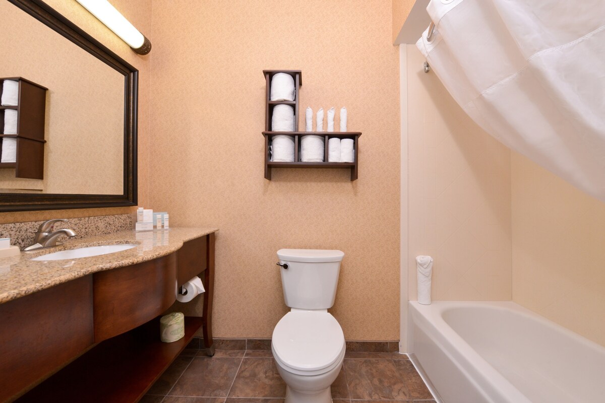 A bathroom with a sink, toilet, and bathtub. There is a shelf with toiletries above the toilet.