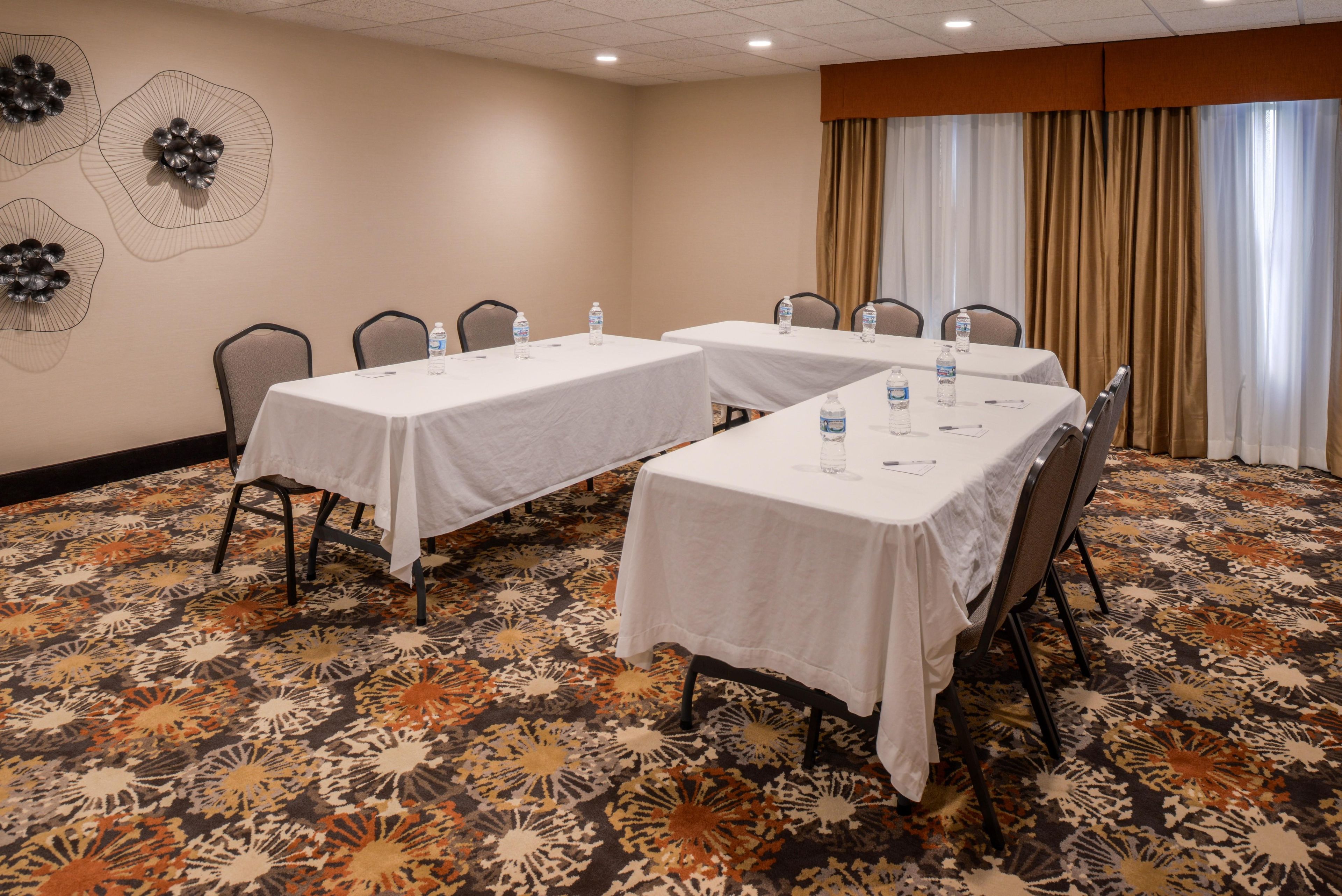 A conference room with two tables, chairs, water bottles, and a patterned carpet.