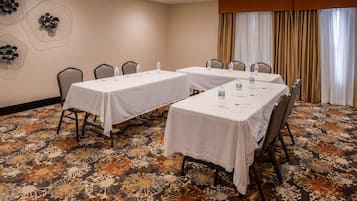 A conference room with two tables, chairs, water bottles, and a patterned carpet.