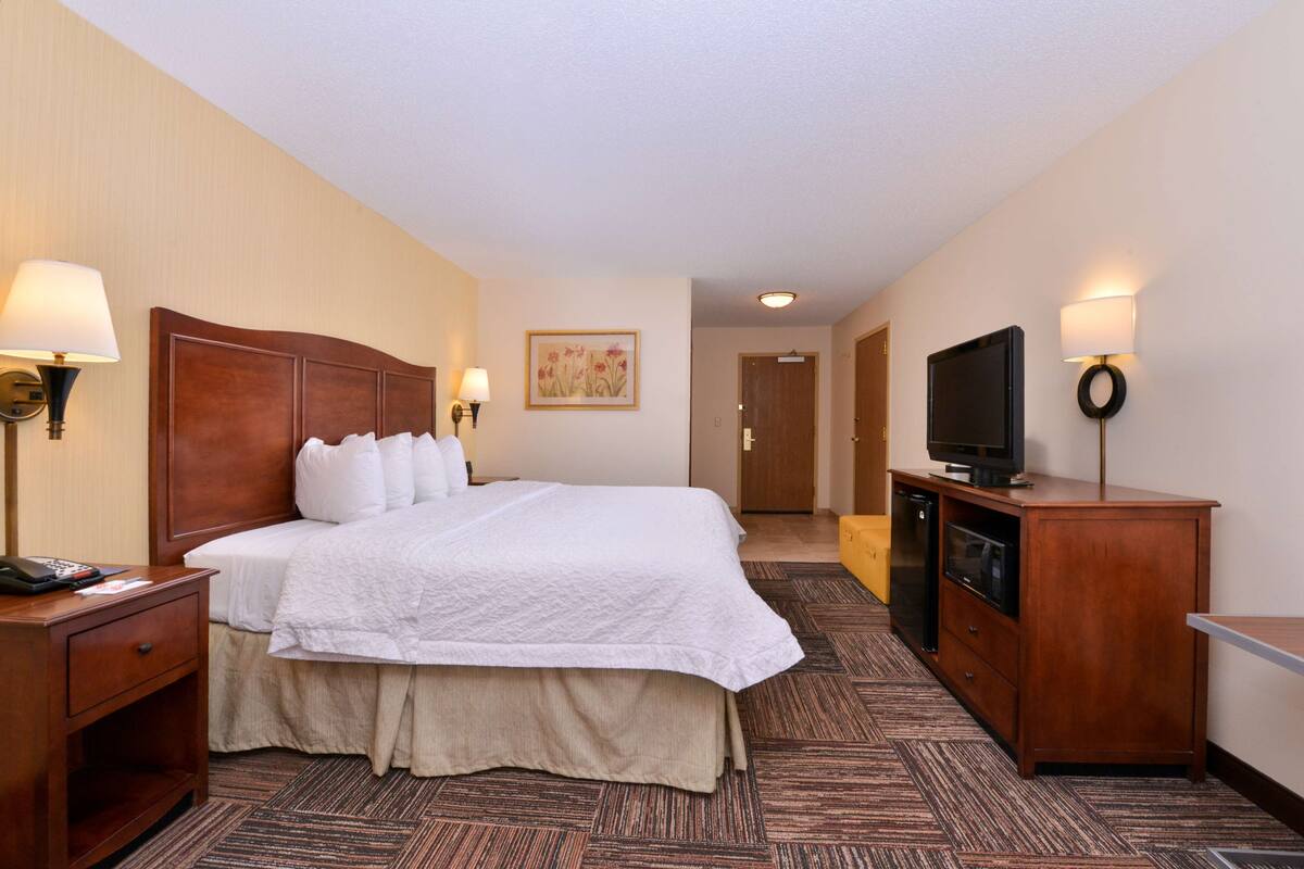 A hotel room with a large bed, bedside lamps, a television on a wooden cabinet, and a door leading to another room.