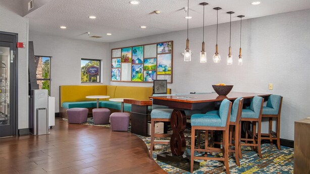 Una moderna hall d'hotel con una reception in legno, opere d'arte colorate al muro e un'area relax con una panca gialla e sedie viola.