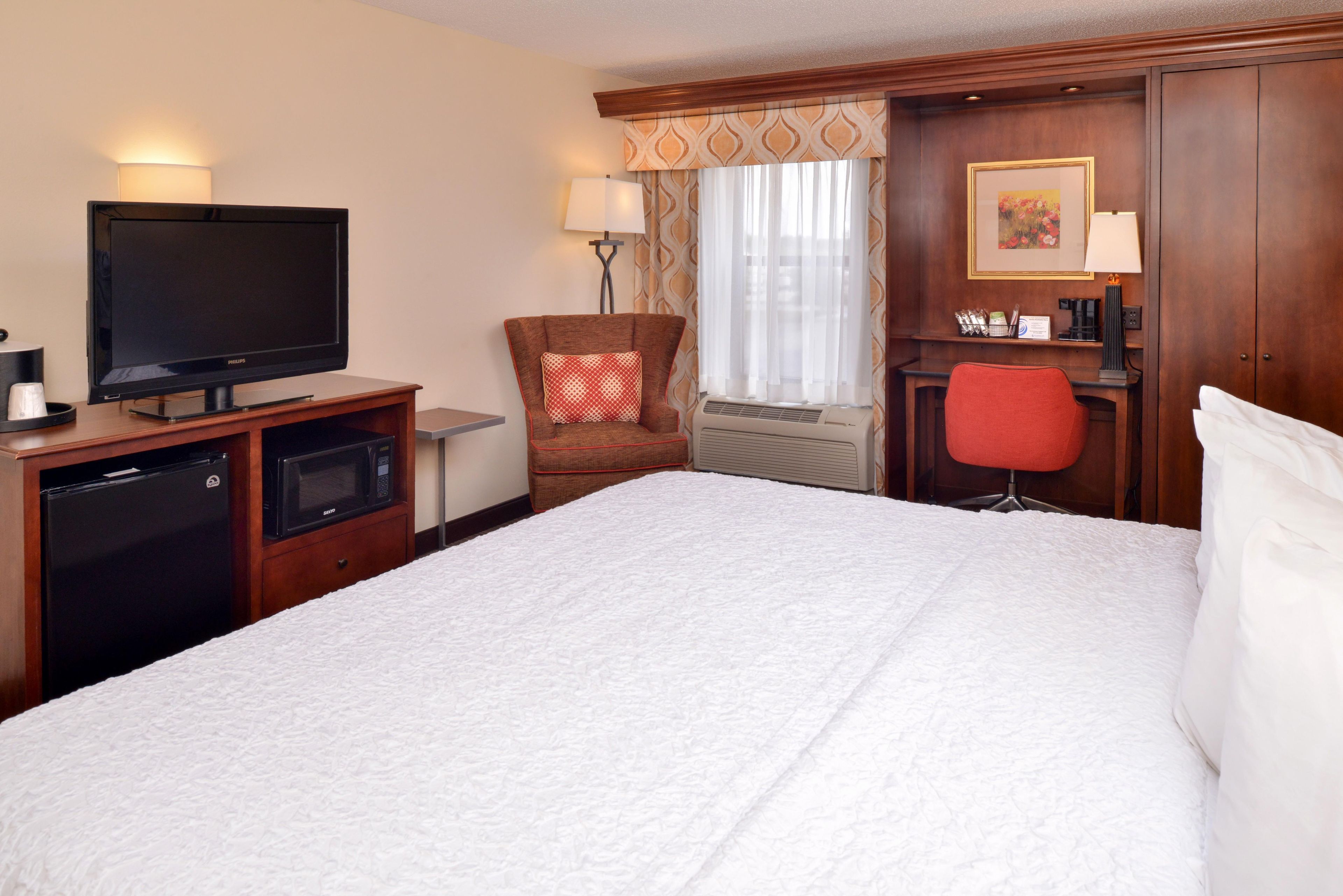 Habitación de hotel con cama, televisión, microondas, una silla roja, escritorio y armario.