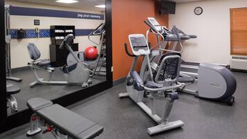A gym with exercise equipment, a bench, and a mirror reflecting the room.