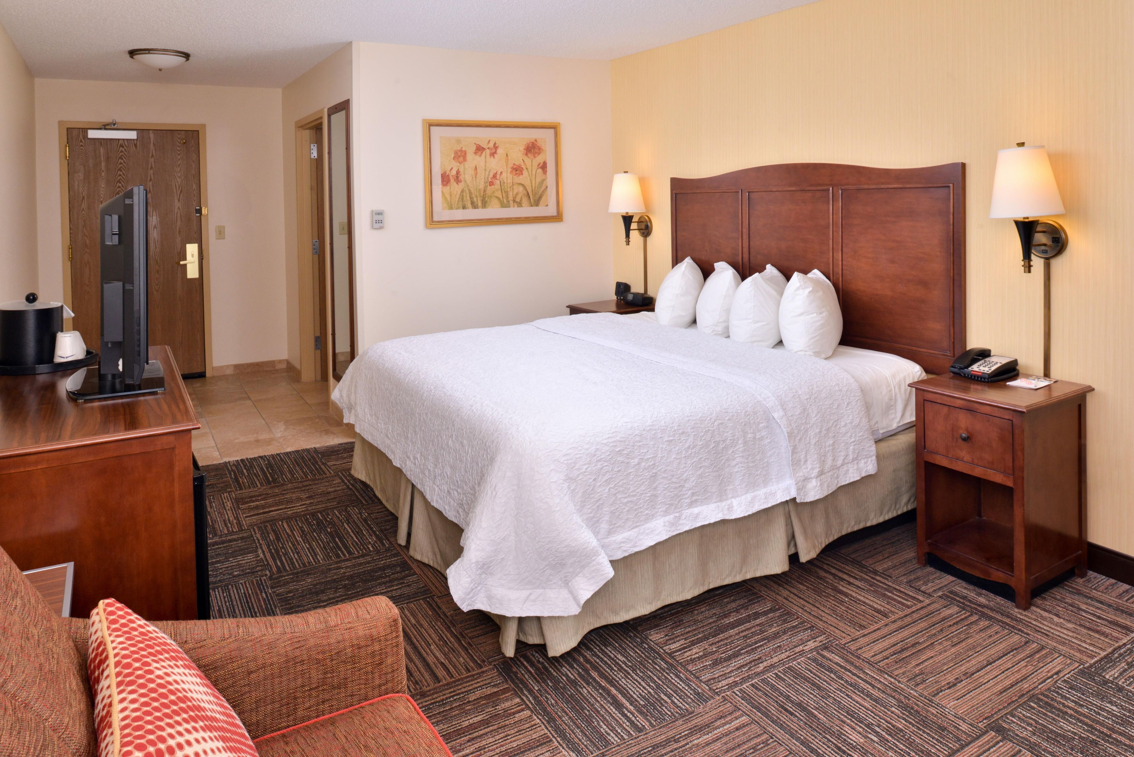 A hotel room with a large bed, two bedside lamps, a desk with a computer, and a chair.