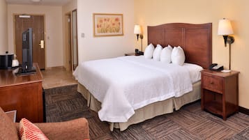 A hotel room with a large bed, two bedside lamps, a desk with a computer, and a chair.