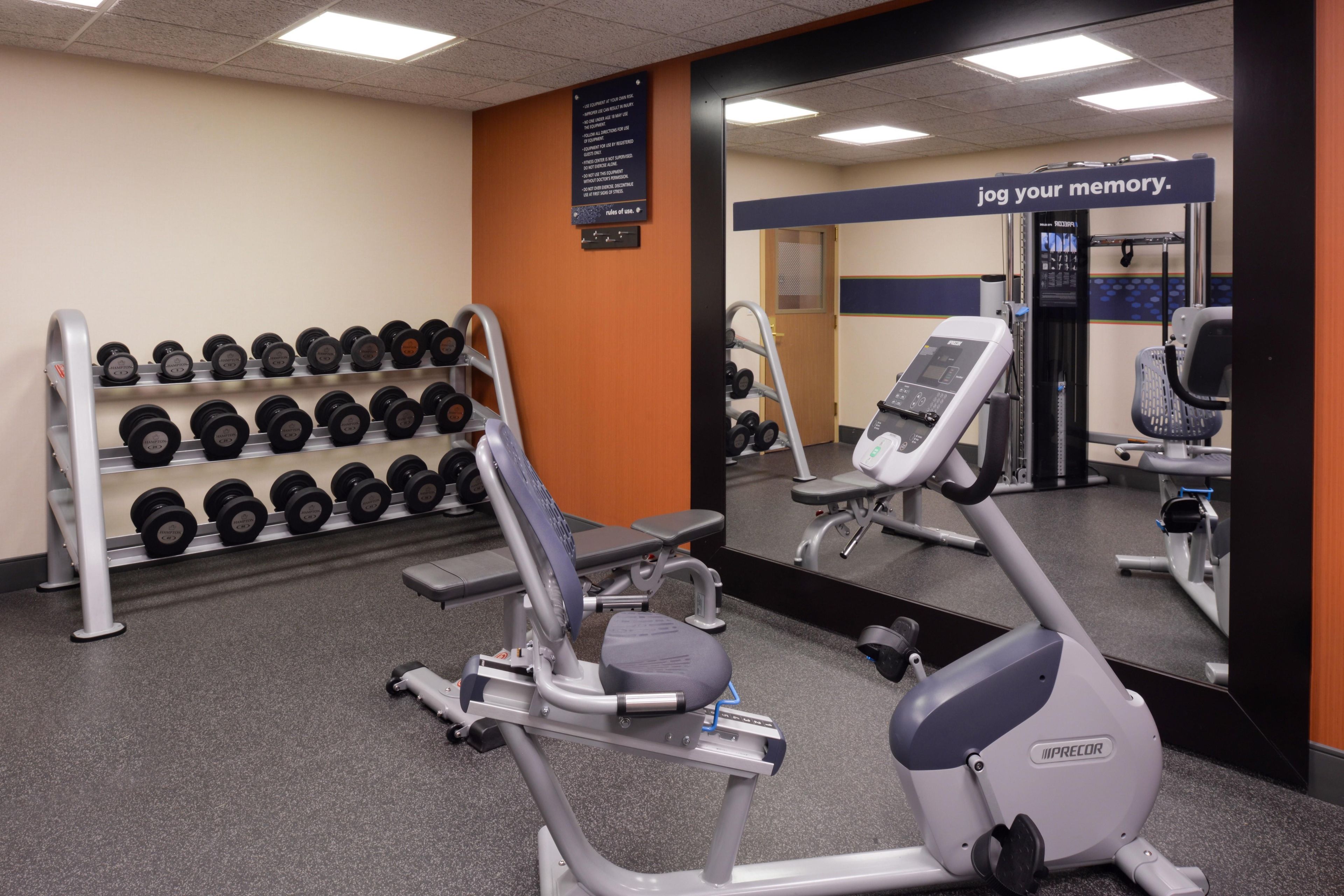 Un gimnasio con equipo de ejercicio, un espejo y un letrero motivacional.