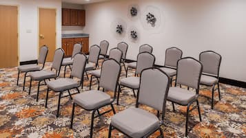 Un salón de conferencias con filas de sillas, alfombra estampada, armarios de madera y obras de arte en la pared.