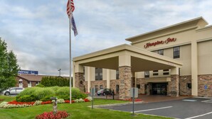Un Hampton Inn con ingresso coperto, un'asta con la bandiera americana e un parcheggio.