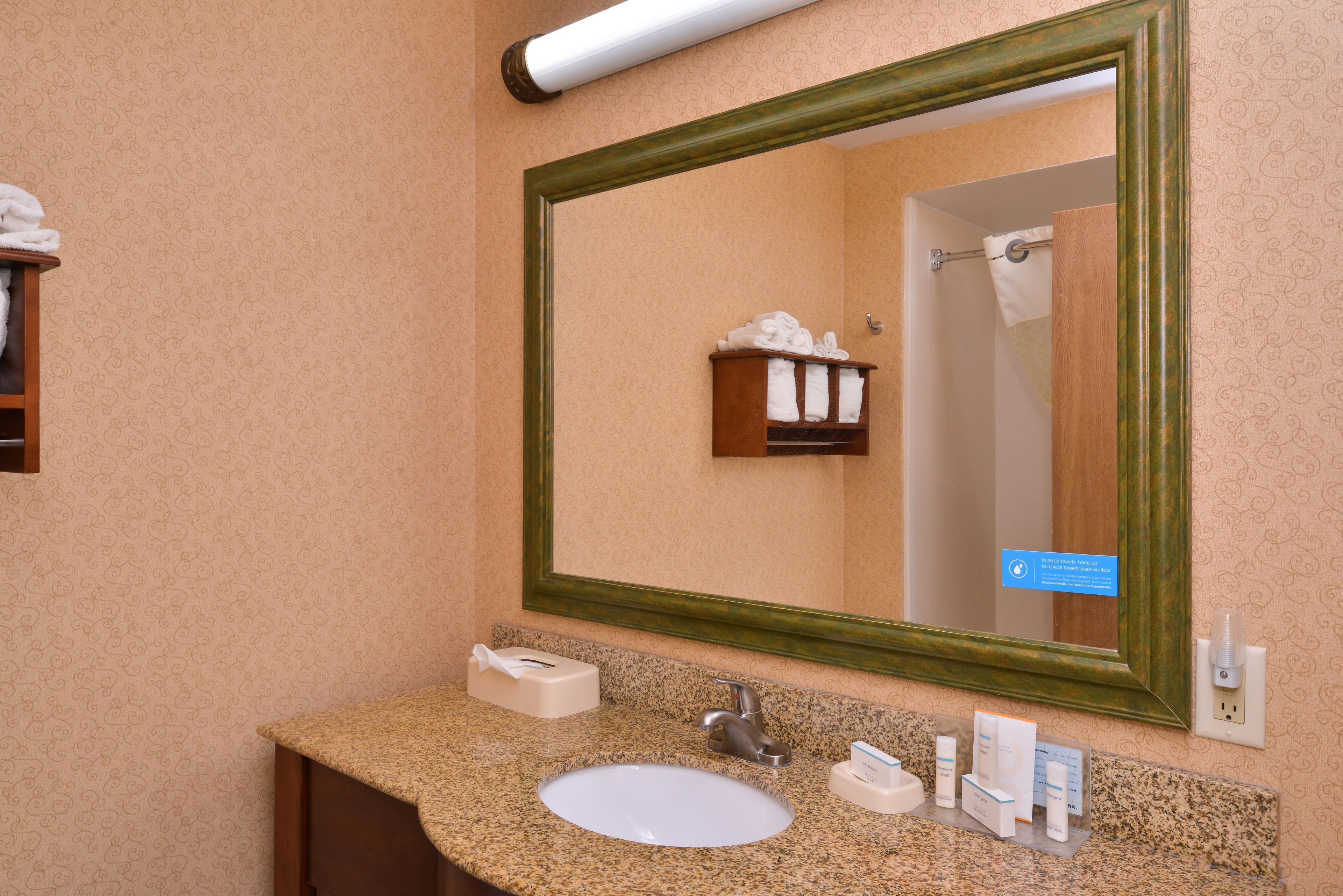 A bathroom with a granite countertop, a white sink, a mirror with a green frame, and a towel rack with folded towels.