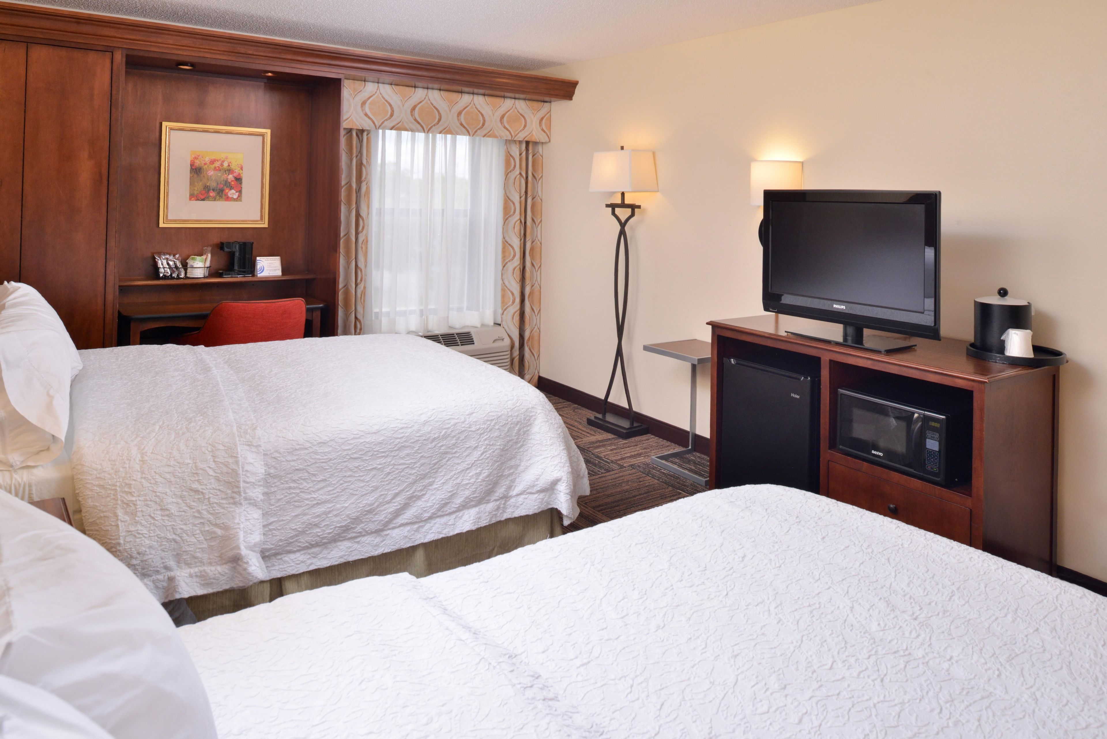 A hotel room with two beds, a desk, a television, a coffee machine, and a refrigerator.