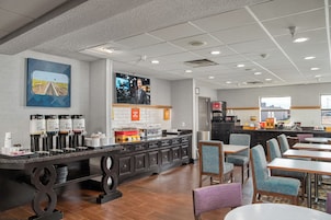 A modern hotel lobby with a coffee station, seating area, and a large TV screen.