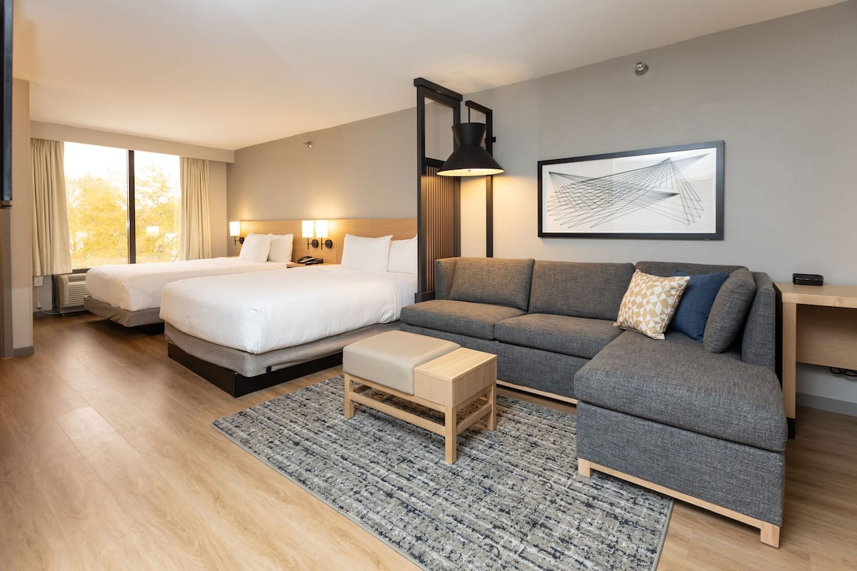 A hotel room with two beds, a sofa, a coffee table, and a large window with curtains.