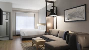Ein modernes Hotelzimmer mit einem Bett, einer Couch, einem Schreibtisch und einem großen Fenster.