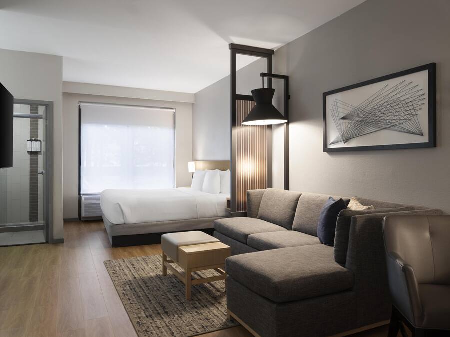 Ein modernes Hotelzimmer mit einem Bett, einer Couch, einem Schreibtisch und einem großen Fenster.