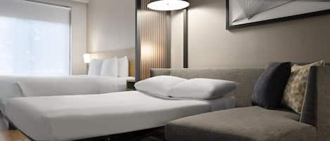 A modern hotel room with a large bed, a sofa, a desk, and a lamp.