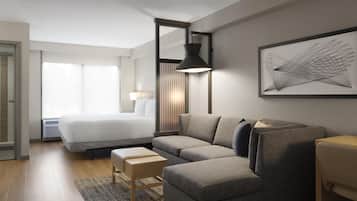 A modern hotel room with a large bed, a gray sofa, a small table, and a wall-mounted lamp.