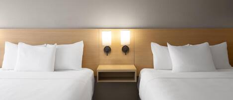 Ein Hotelzimmer mit zwei Betten, einem hölzernen Kopfteil und einem Nachttisch mit Lampe.