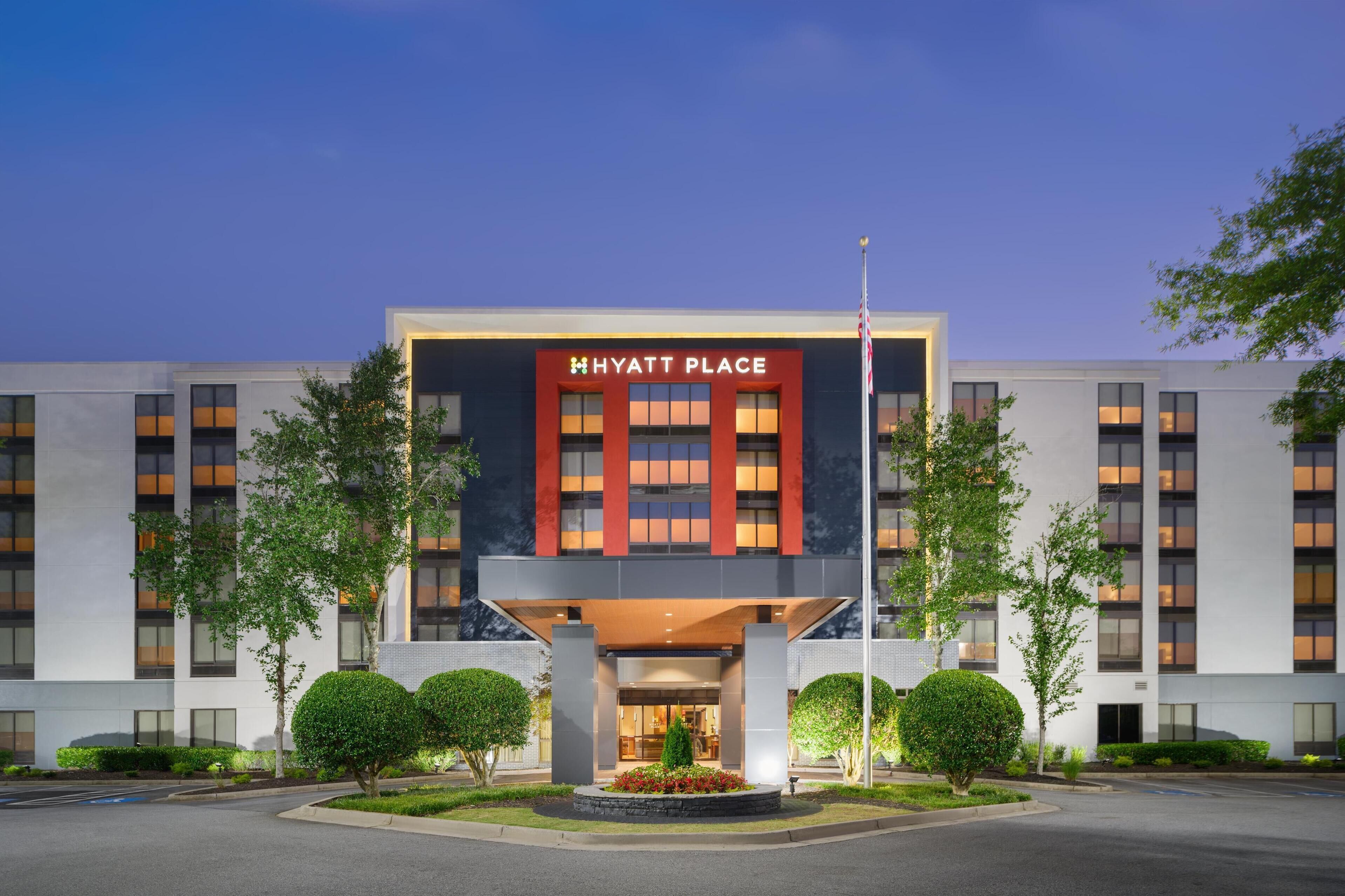 A modern hotel with a prominent 'Hyatt Place' sign, featuring a symmetrical facade with large windows and a central entrance.