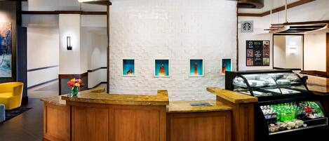 A reception area with a curved wooden counter, a white tiled wall with small windows, and a beverage display case.
