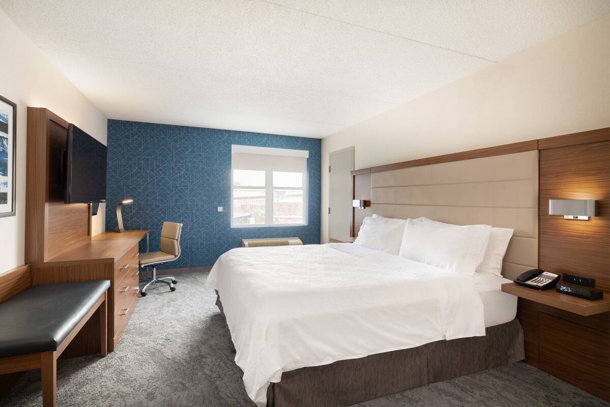 A hotel room with a bed, desk, chair, and a TV.