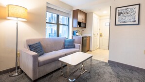 A modern living room with a sofa, a coffee table, a floor lamp, and a kitchen area in the background.