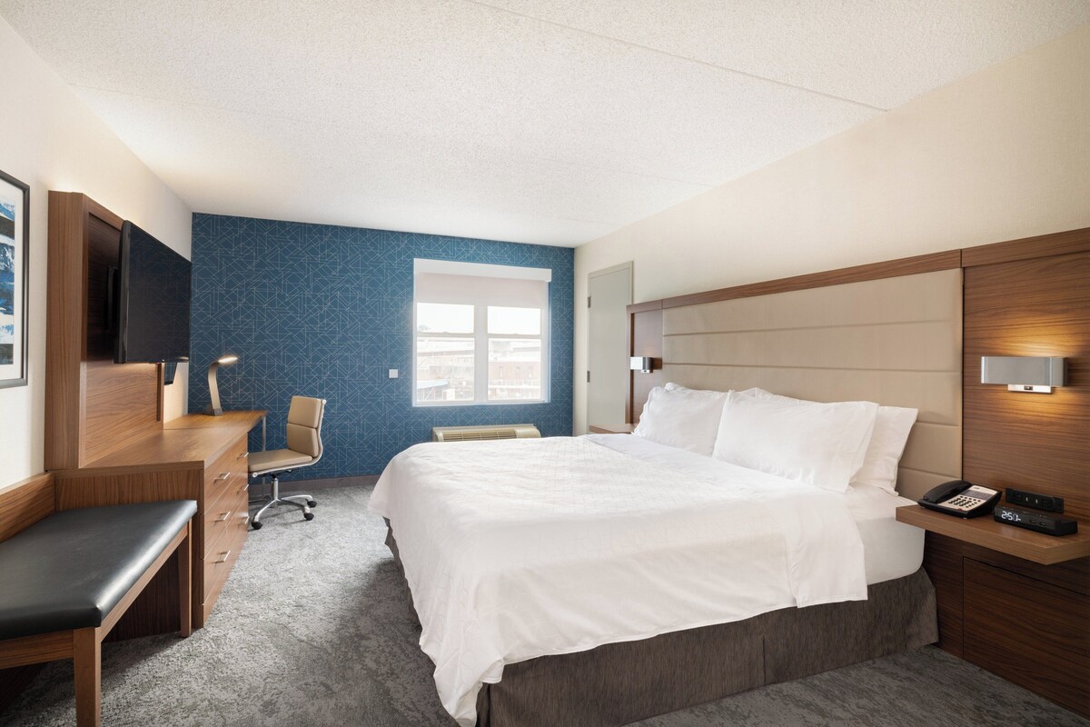 A hotel room with a bed, desk, chair, and a TV.