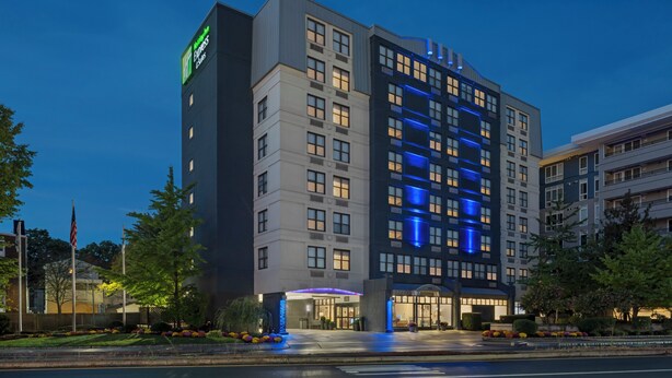 A multi-story hotel with a modern design, featuring a prominent entrance with a blue-lit canopy and a visible American flag.