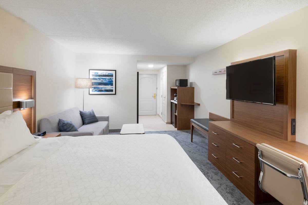 A hotel room with a large bed, a desk with a flat-screen TV, a sofa, a lamp, and a painting on the wall.