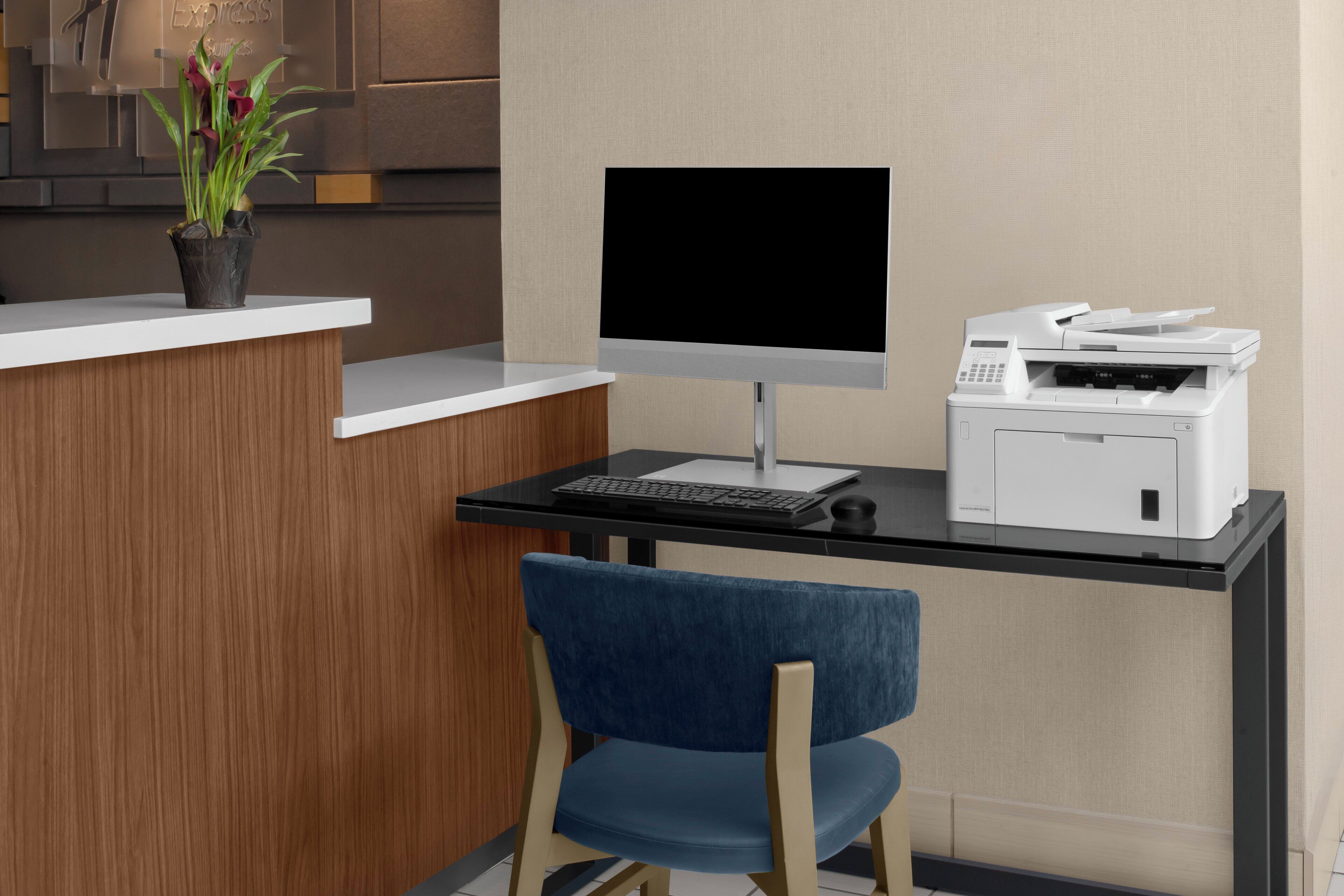 Un mostrador de recepción con un monitor de computadora, teclado e impresora. Hay una silla azul frente al mostrador.