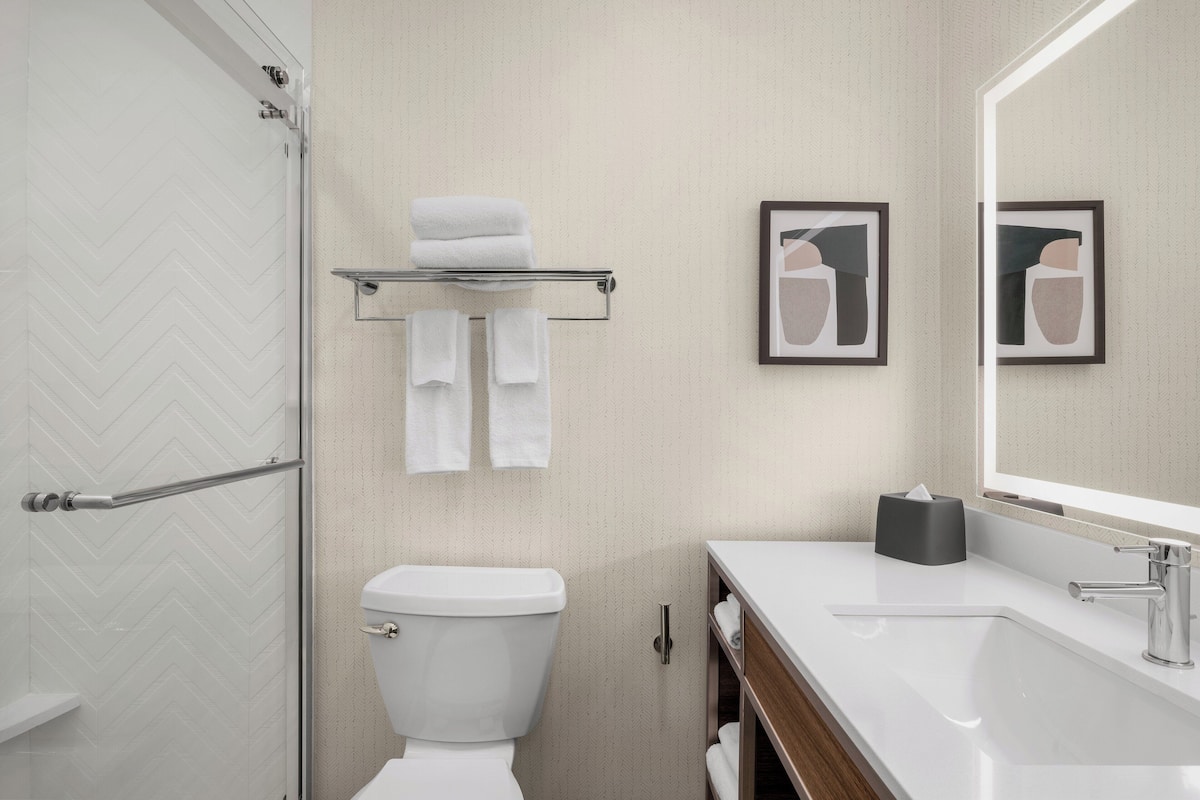 A modern bathroom with a white toilet, a glass shower enclosure, a white sink with a mirror, and two framed pictures on the wall.