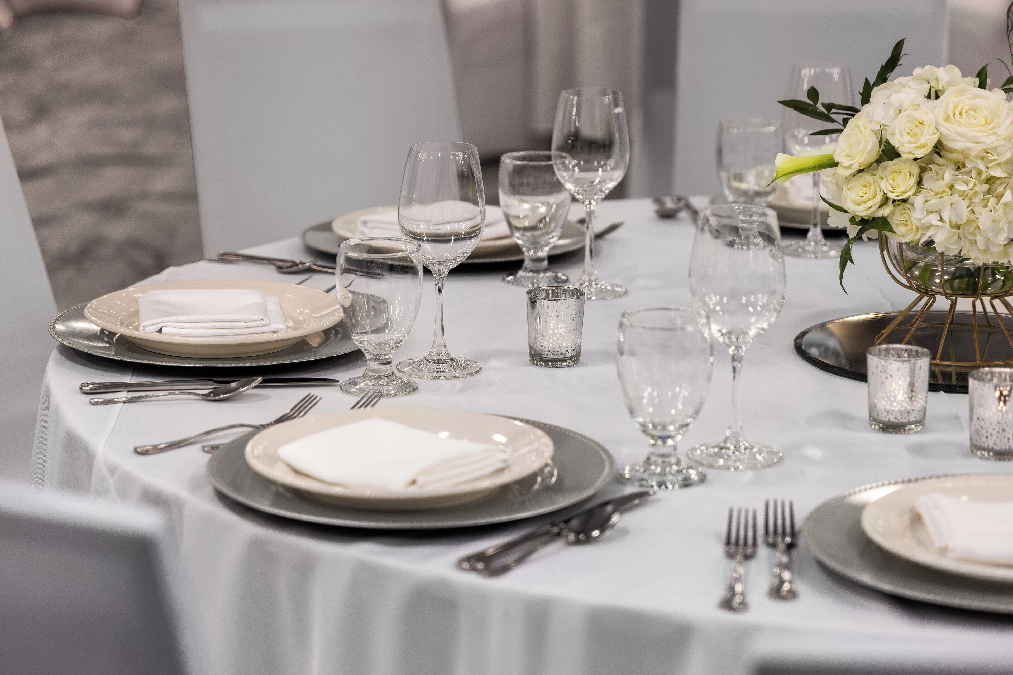 A table set for a formal dinner with white plates, silverware, and clear glassware.