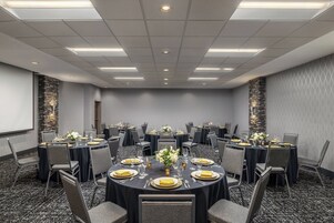 A conference room with round tables, chairs, and a projector screen.