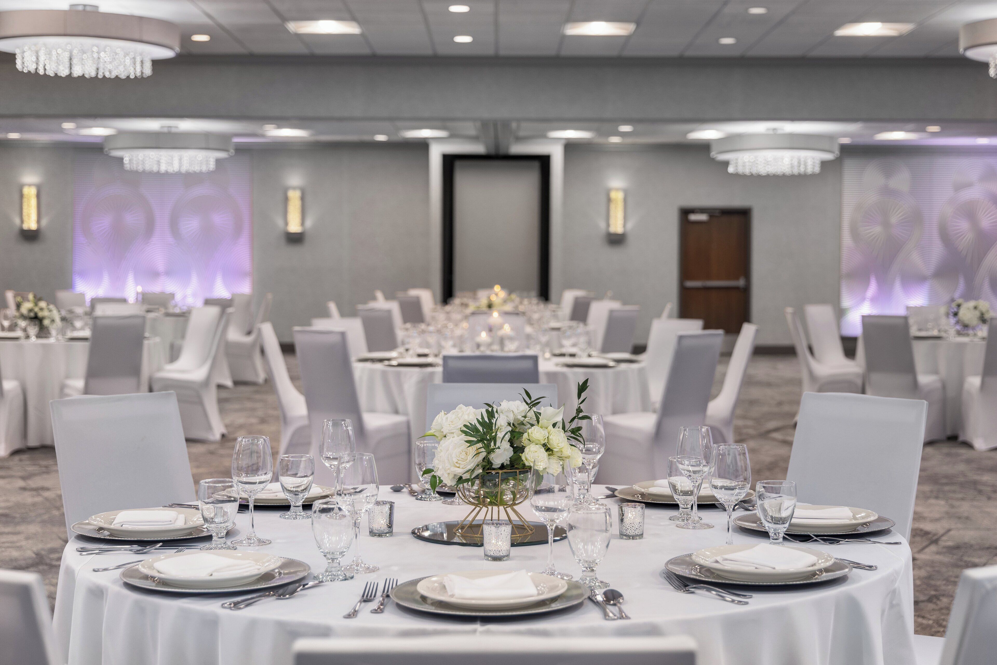 Une salle de banquet avec des tables rondes dressées pour le repas, chacune étant recouverte d’une nappe blanche et agrémentée de couverts et de verres.