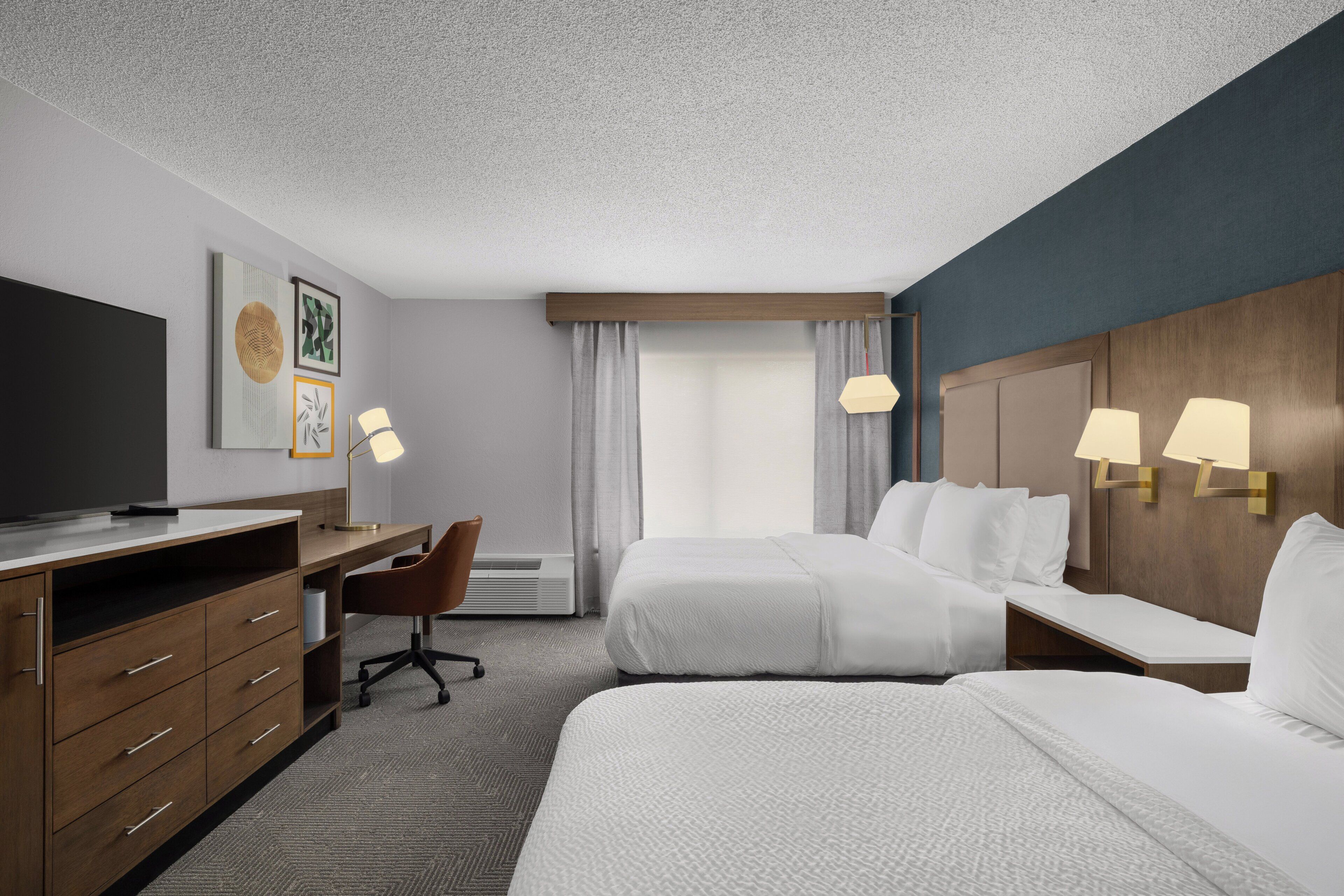 Een hotelkamer met een bed, een bureau met stoel, een televisie en een lamp.
