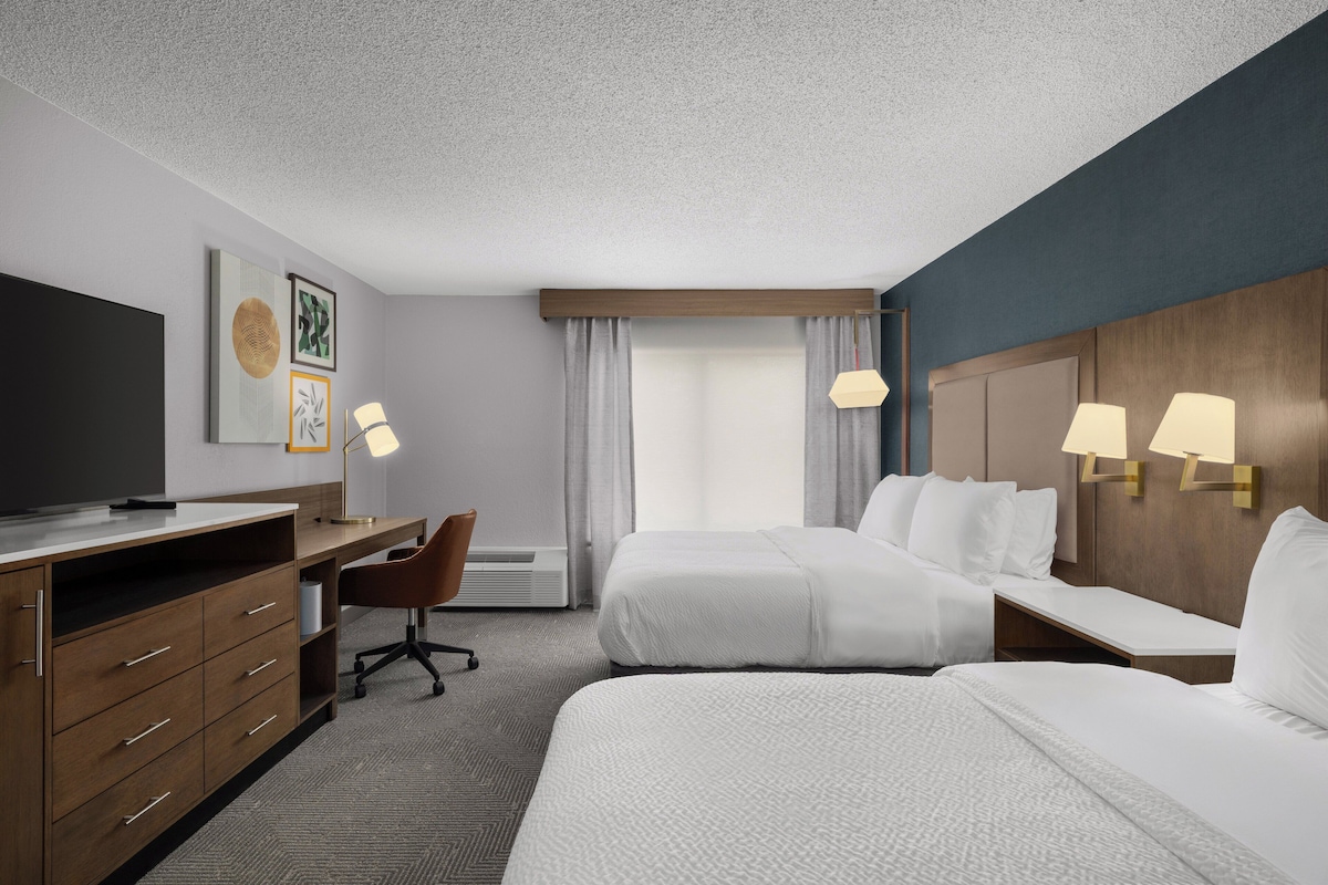 Una habitación de hotel con cama, escritorio, silla, televisión y lámpara.