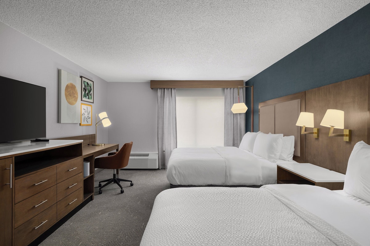 A hotel room with a bed, a desk with a chair, a TV, and a lamp.