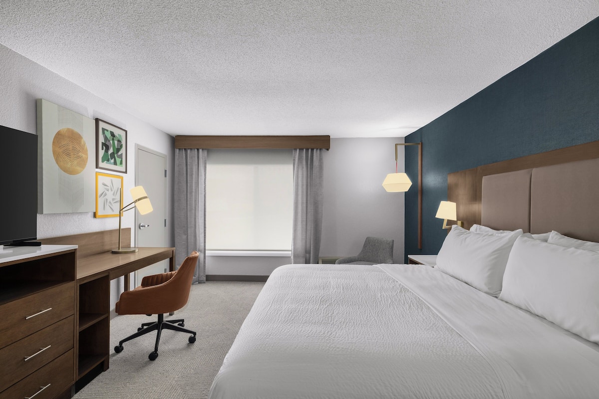 A hotel room with a bed, desk, chair, and two lamps.